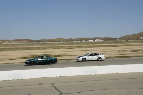 1995 Ford Taurus - Two sedans are seen on a racetrack under a clear blue sky.