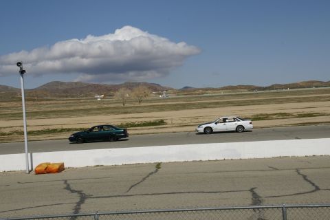 1995 Ford Taurus - Two sedans compete on a racetrack under a partly cloudy sky.