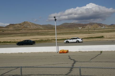 1995 Ford Taurus - Two sedans are seen racing on a track under a partly cloudy sky.