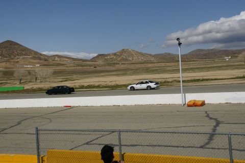 1995 Ford Taurus - Two sedans are on a race track with hills and clouds in the background.