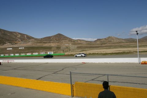 1995 Ford Taurus - A black car and a white car are on a racetrack with a person watching in the foreground.
