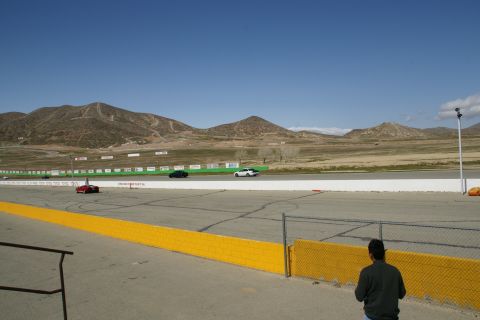 1995 Ford Taurus - A race track scene with multiple vehicles visible on the track under a clear blue sky.