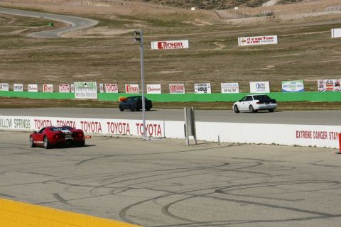 1995 Ford Taurus - A red sports car is seen on a race track with other vehicles in the background.