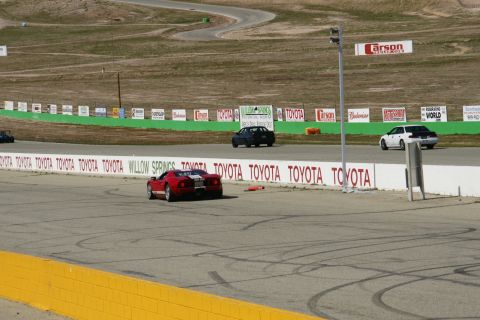 1995 Ford Taurus - A red sports car navigates a race track, with other vehicles and sponsor banners visible.
