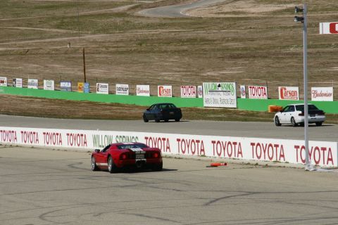 1995 Ford Taurus - A red sports car navigates a turn on a race track, with other vehicles visible in the background.