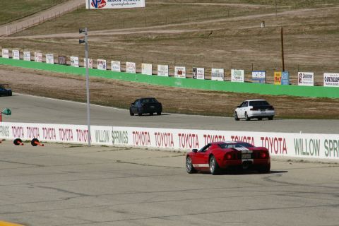 1995 Ford Taurus - A red sports car is on a race track with other vehicles in the distance.
