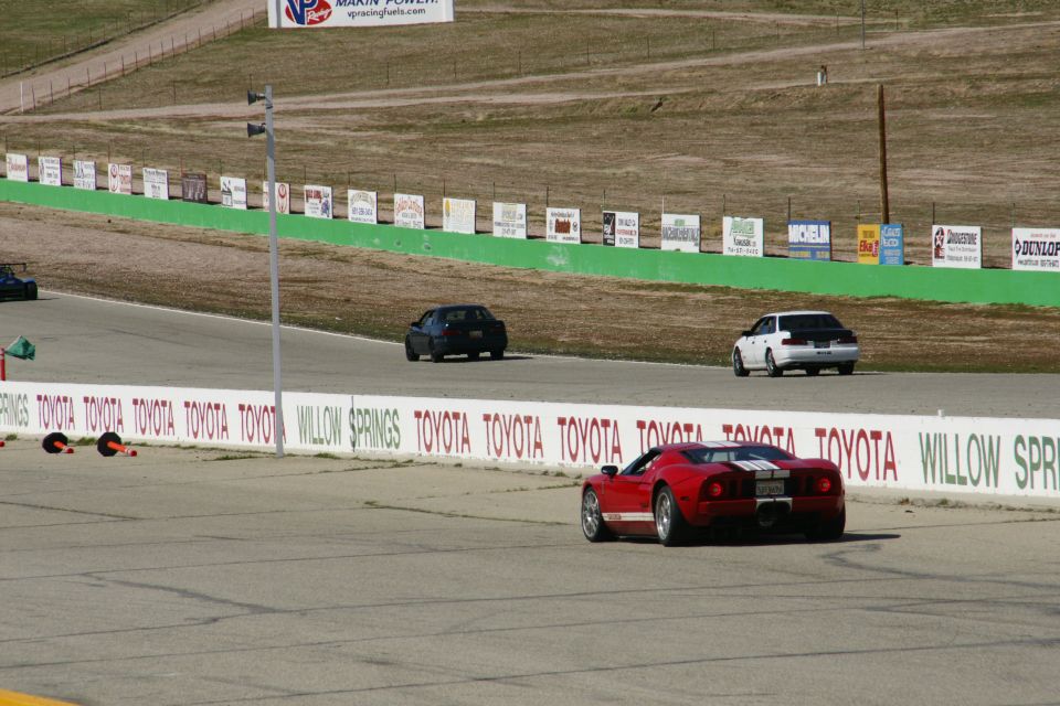 Red sports car with white stripes on a race track, other cars in background