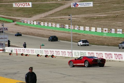 1995 Ford Taurus - A red sports car is on the track at Willow Springs, with other vehicles and Toyota signage in the background.