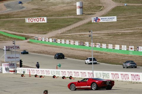 1995 Ford Taurus - A red sports car is on the track at Willow Springs, with other vehicles and sponsor signs visible.