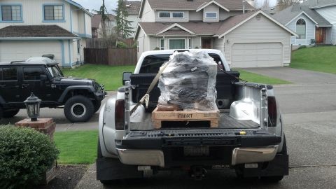 2008 Jeep Wrangler - A black Jeep Wrangler is parked next to a pickup truck loaded with a wrapped engine on a wooden pallet.
