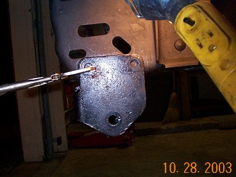 1986 Ford Bronco - A close-up view shows a metal bracket being attached to a vehicle's frame with a tool.