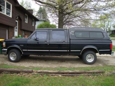 1999 Ford Ranger - A black crew cab pickup truck with a camper shell is parked in a driveway next to a brown house.