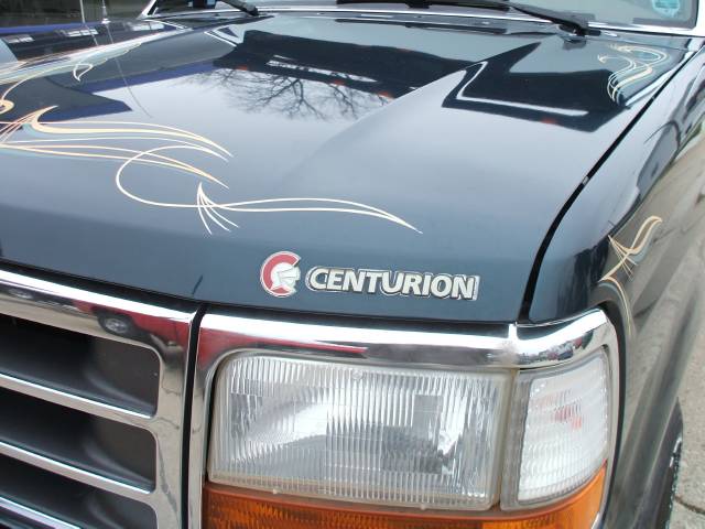 Dark blue truck hood with chrome grille, headlights, and pinstripe graphics. Centurion badge is visible