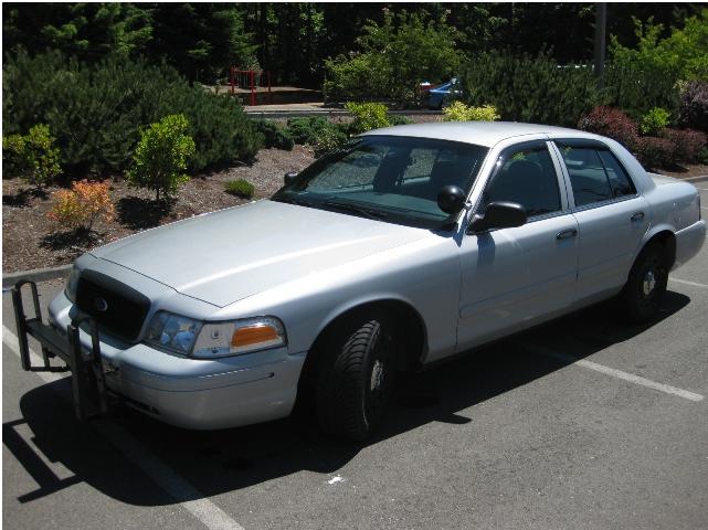 Silver Ford Crown Victoria sedan with front push bar and black steel wheels, parked in a lot
