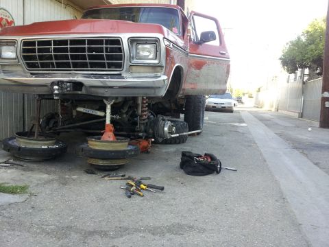 1978 Ford Bronco - A red pickup truck is undergoing maintenance with its front end raised and wheels off.