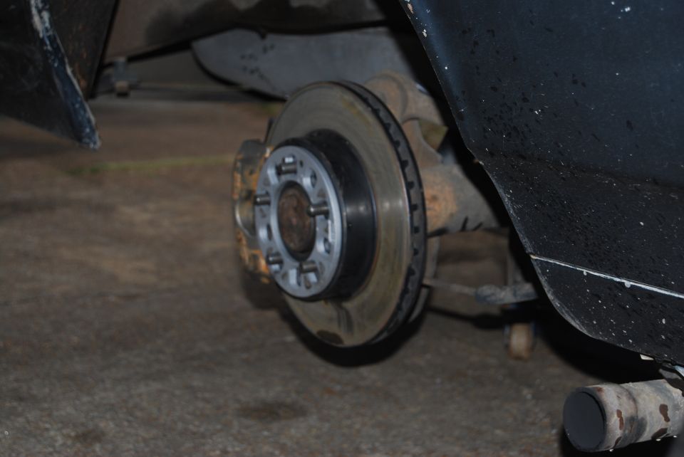 Close-up of a vehicle's rear brake rotor and caliper assembly, showing the hub and lug nut holes