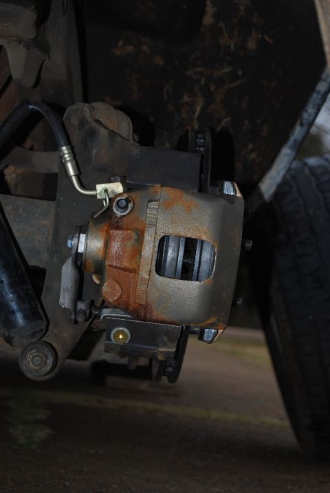 1975 Ford Ranchero - Close-up view of a rusty rear disk brake caliper and associated suspension components.