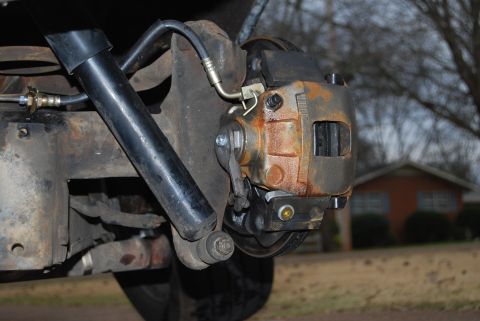 1975 Ford Ranchero - The rear brake caliper and shock absorber are visible, with a house and trees in the background.