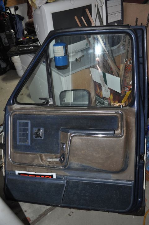 1986 Ford Bronco - Interior of a car door, dark blue and brown upholstery with chrome trim. A small sticker is visible near the bottom.
