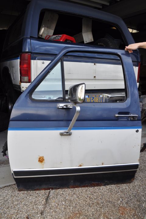 1986 Ford Bronco - Removed door from a 1986 Ford Bronco, with rust spots visible. Another Bronco is in the background.