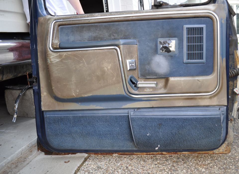 Interior door panel with brown and blue fabric, showing a window crank, door handle, and air vent