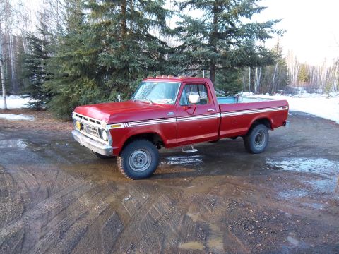 1978 Ford F-250 - A red pickup truck sits on a muddy road with trees and snow in the background.