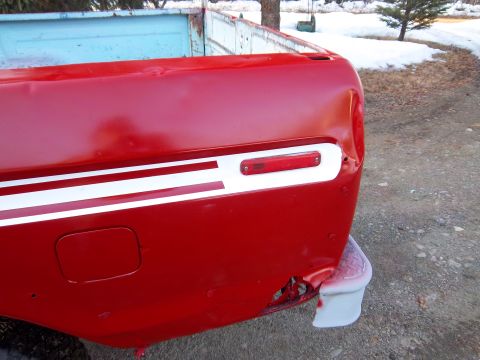 1978 Ford F-250 - Rear corner of a red pickup truck bed, showing damage and a white stripe detail.