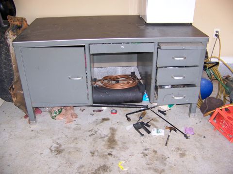 2000 Jeep Wrangler - A cluttered garage scene features a metal desk, various tools scattered on the floor, and a spare tire to the left.