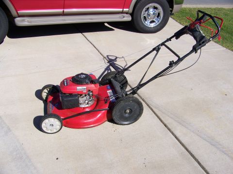 2000 Jeep Wrangler - A red push lawn mower is parked on a concrete driveway next to a red SUV.
