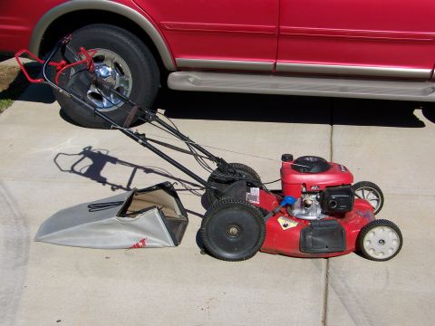 2000 Jeep Wrangler - A red lawn mower and a red SUV are parked on a concrete surface. The lawn mower's grass bag is detached.
