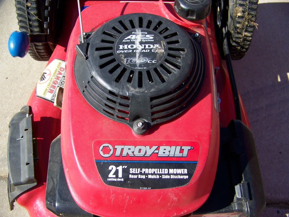 Red Troy-Bilt 21-inch self-propelled mower with Honda 160cc engine, close-up on deck and engine