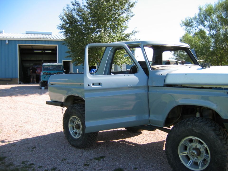 1978 Ford Bronco body panels, door removed, parked outside garage with another Bronco inside