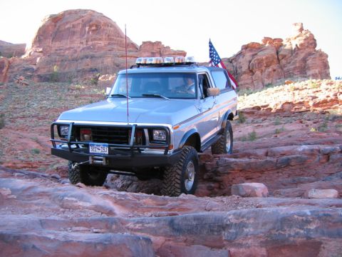 1978 Ford Bronco - A silver 1978 Ford Bronco navigates a challenging rocky trail under a bright sky.