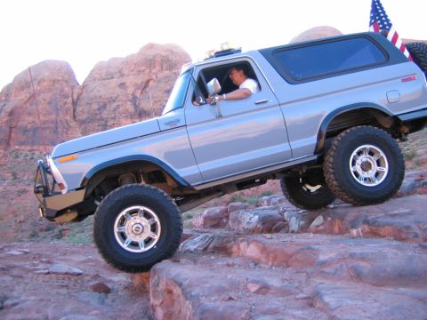 1978 Ford Bronco - A silver 1978 Ford Bronco navigates a rocky off-road course with a driver behind the wheel.