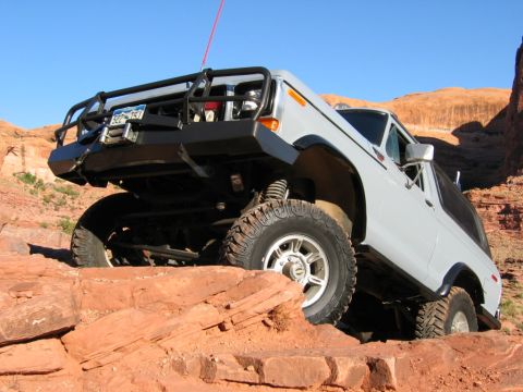 1978 Ford Bronco - This SUV is navigating a challenging rocky terrain under a clear blue sky.