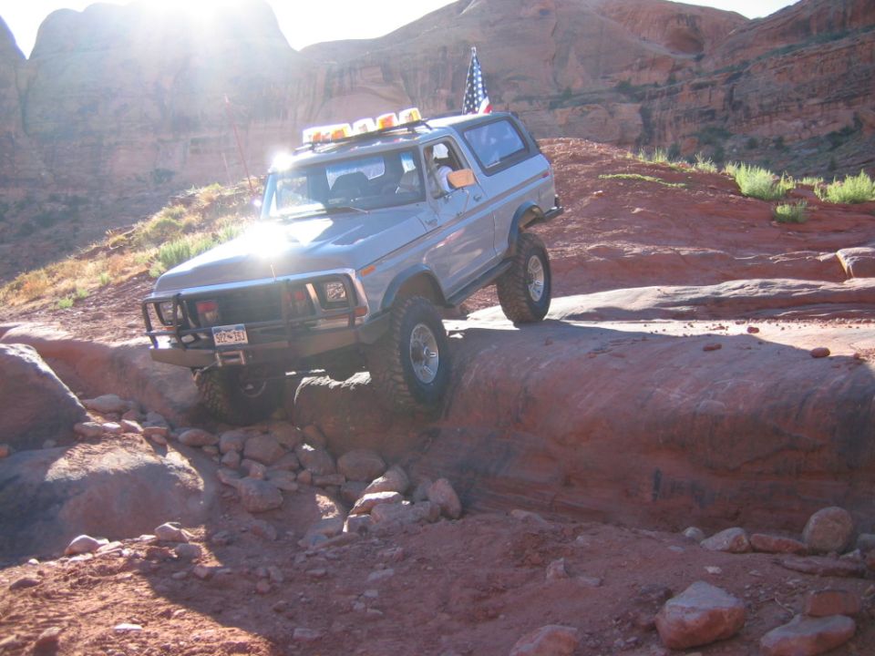 Silver Ford Bronco 4x4 climbing red slickrock with roof light bar and flag