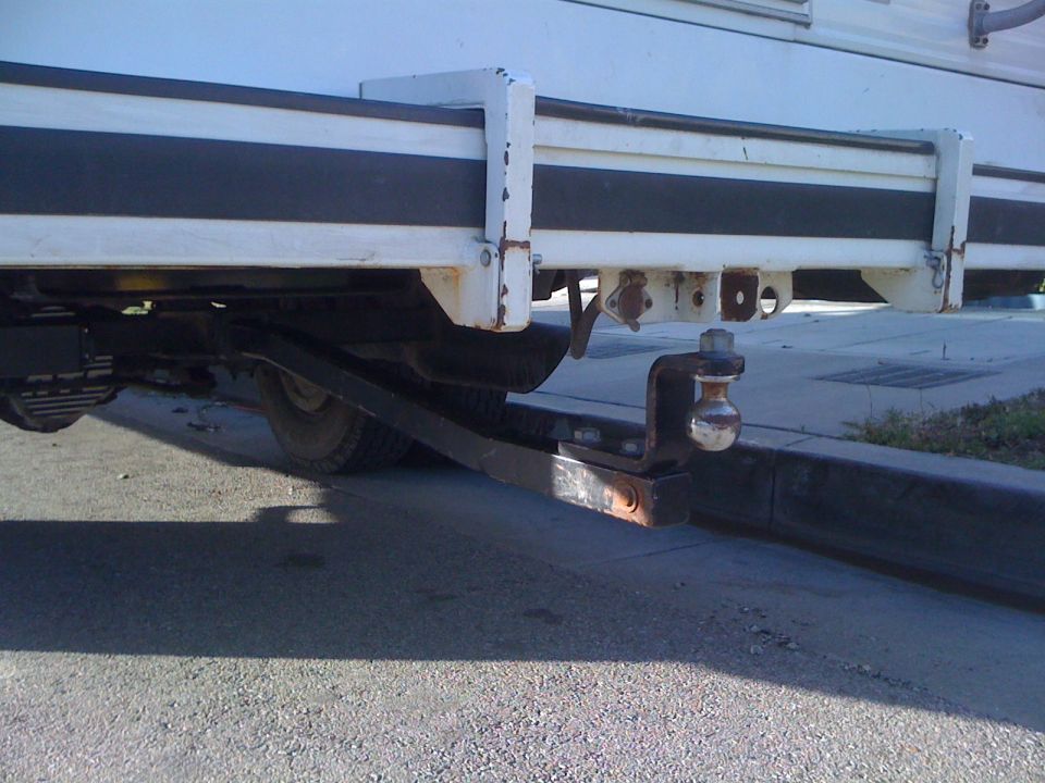 Receiver hitch extension with chrome tow ball under the rear of a white RV with black stripe