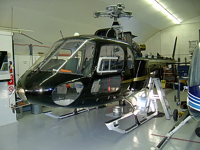 Black helicopter on skids in a hangar with step ladder beside it