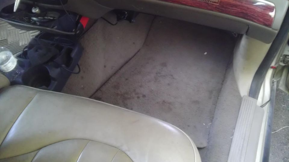 Passenger side floor and lower dashboard area of a car. There's a water bottle and some clutter on the floor