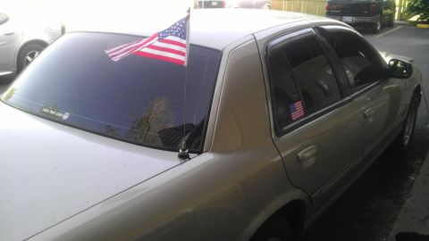 2000 Mercury Grand Marquis - A tan 2000 Mercury Grand Marquis is seen from the rear quarter with an American flag attached to its antenna and a sticker on the rear wind…