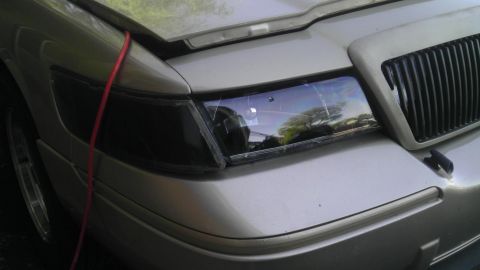 2000 Mercury Grand Marquis - The front corner of a silver 2000 Mercury Grand Marquis is visible, showing a blacked-out headlight and a vertical grille.