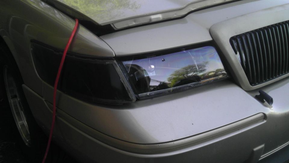 Silver 2000 Mercury Grand Marquis front corner with a blacked-out headlight and vertical grille