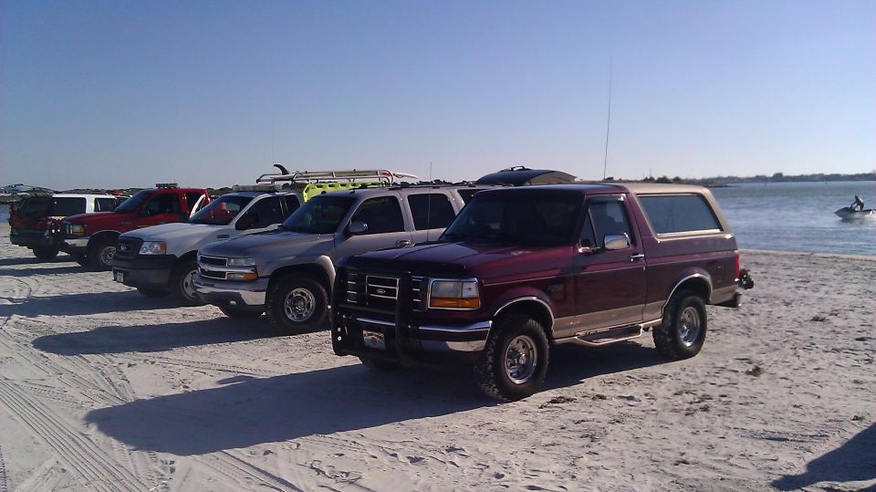 Maroon 1996 Ford Bronco with tan top on beach, 3/4 front view