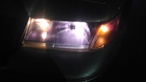 2000 Mercury Grand Marquis - The front headlight assembly of a 2000 Mercury Grand Marquis is visible, with the headlight illuminated.