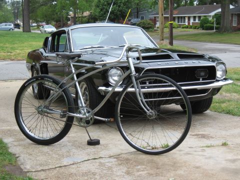 1994 Ford Bronco - A vintage bicycle stands in front of a classic black Ford Mustang.