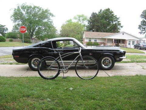 1994 Ford Bronco - A classic black 1967 Ford Mustang Shelby GT500 is parked next to a bicycle on a suburban street.