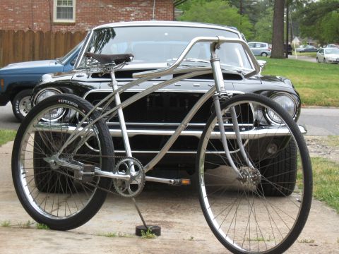 1994 Ford Bronco - A custom cruiser bicycle is parked in front of a black classic car, with a blue SUV visible behind it.