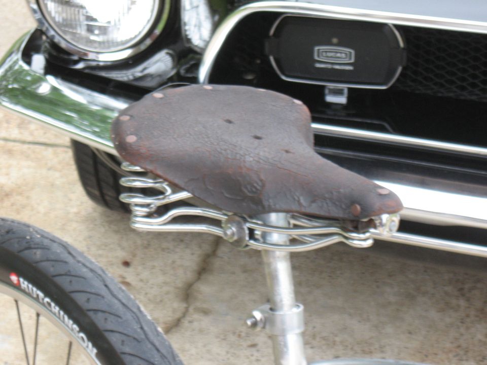 Brown leather bicycle seat with chrome springs, in front of a black car grille