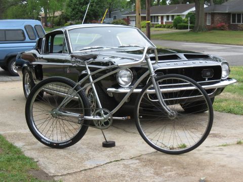 1994 Ford Bronco - A vintage bicycle is positioned before a classic black Ford Mustang, with a blue pickup truck visible to the left.