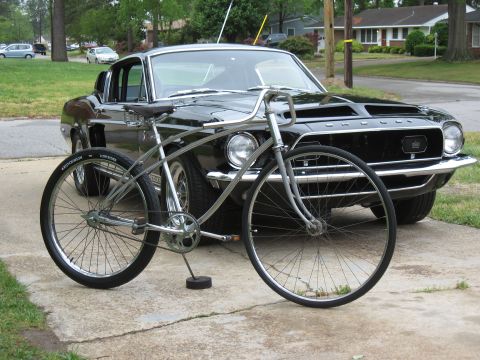 1994 Ford Bronco - A classic black Ford Mustang is parked behind a vintage bicycle on a driveway.